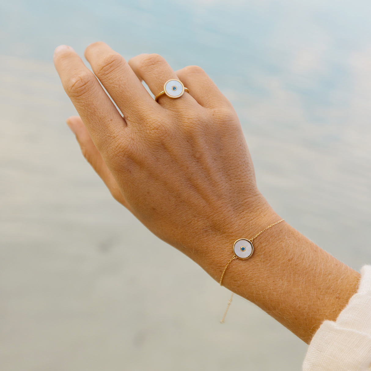 Woman's hand modelling a mother of pearl bracelet and ring on a blurred natural background.