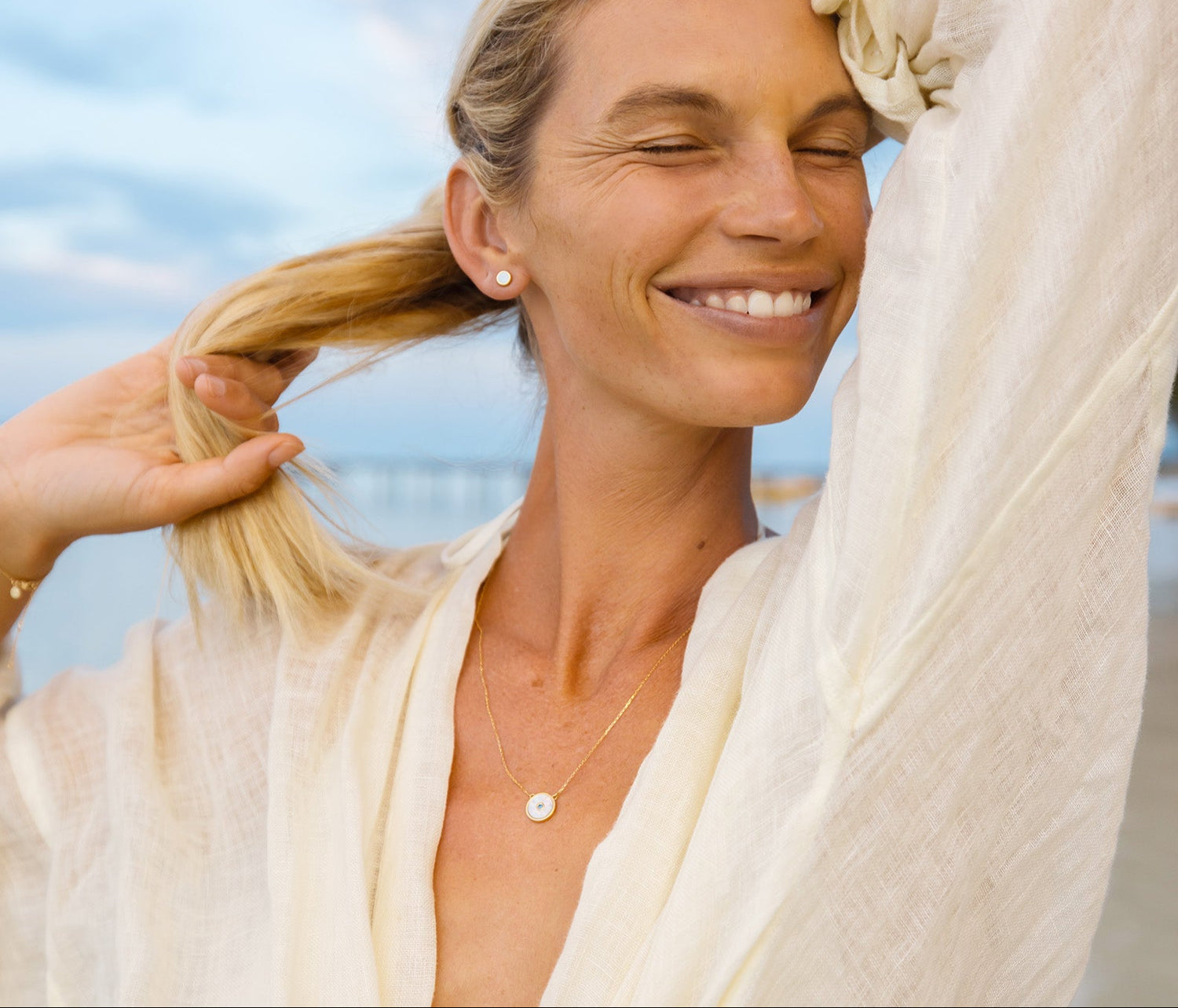 Woman with blonde hair smiling outdoors with a light blue sky background