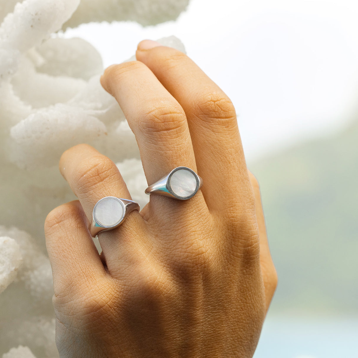 Hand holding white coral modelling 2 silver mother of pearl rings