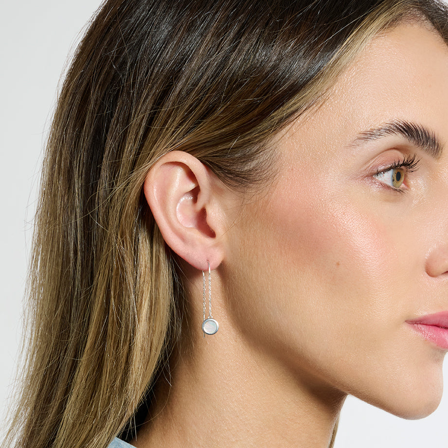 Model facing side on to the camera wearing silver mother of pearl dangle earrings on a white background