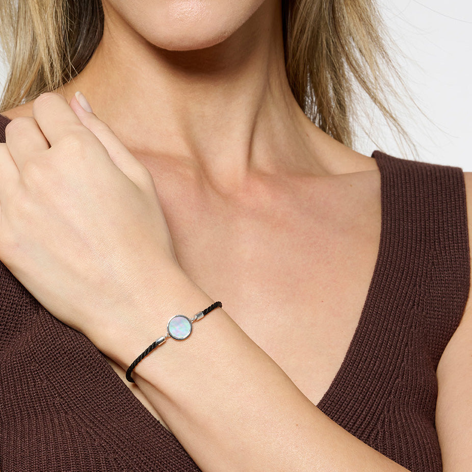 Model wearing a brown tank top and a black silk cord bracelet with a mother of pearl disc in the middle