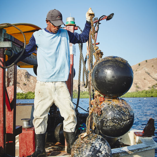 Person on a boat with large black ballast stones in a body of water with mountains in the background
