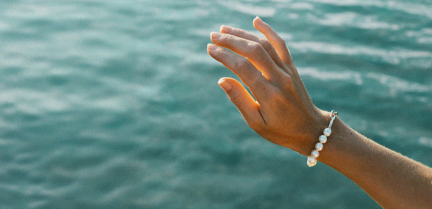 Hand wearing a pearl bracelet with a blurred ocean background