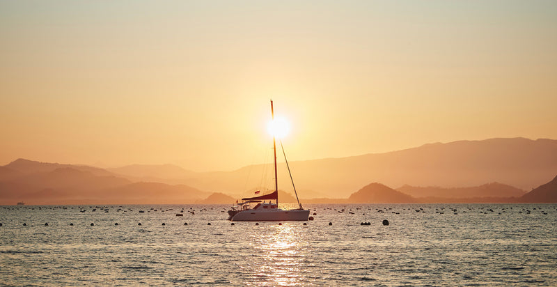 Yacht sailing under the golden sunset with rolling mountains in the background