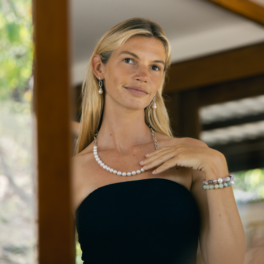 Woman wearing a pearl necklace and bracelet with a blurred outdoor background