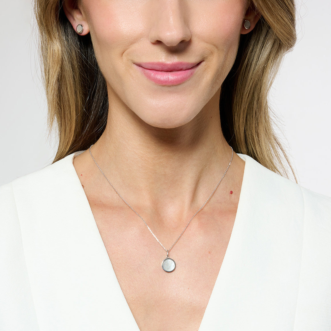 Model wearing silver necklace with a white blazer on a grey white backdrop