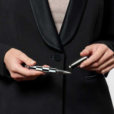 A person in a black jacket holding a pen with a mother of pearl finish.
