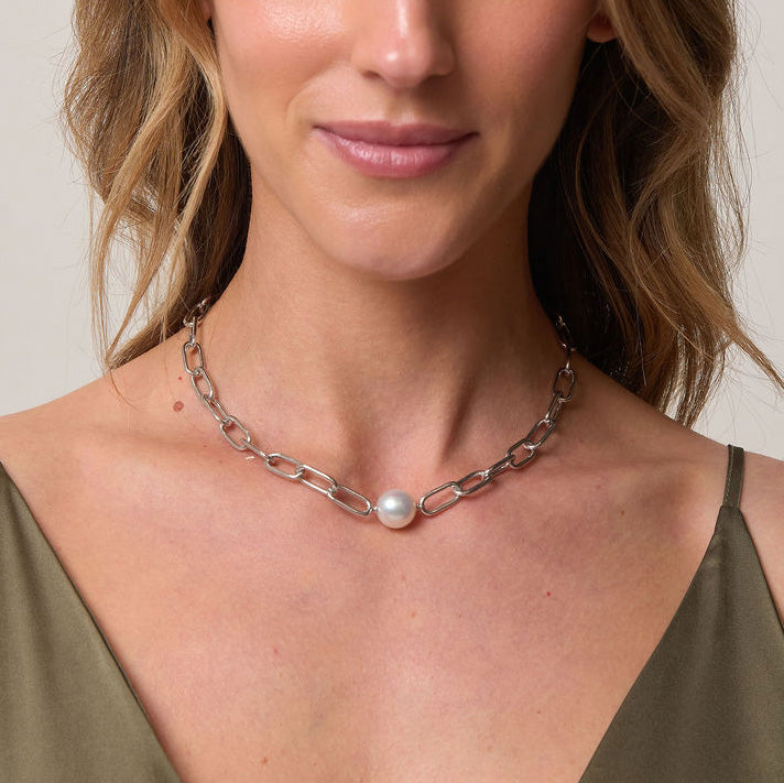 Woman wearing a silver chain necklace with a pearl against a neutral background