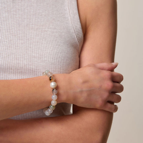 Person wearing white beads with a pearl bracelet on a neutral background