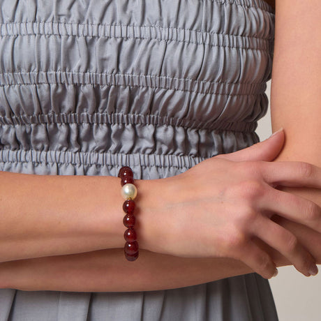 Person wearing a bracelet with red beads with a pearl on a neutral background