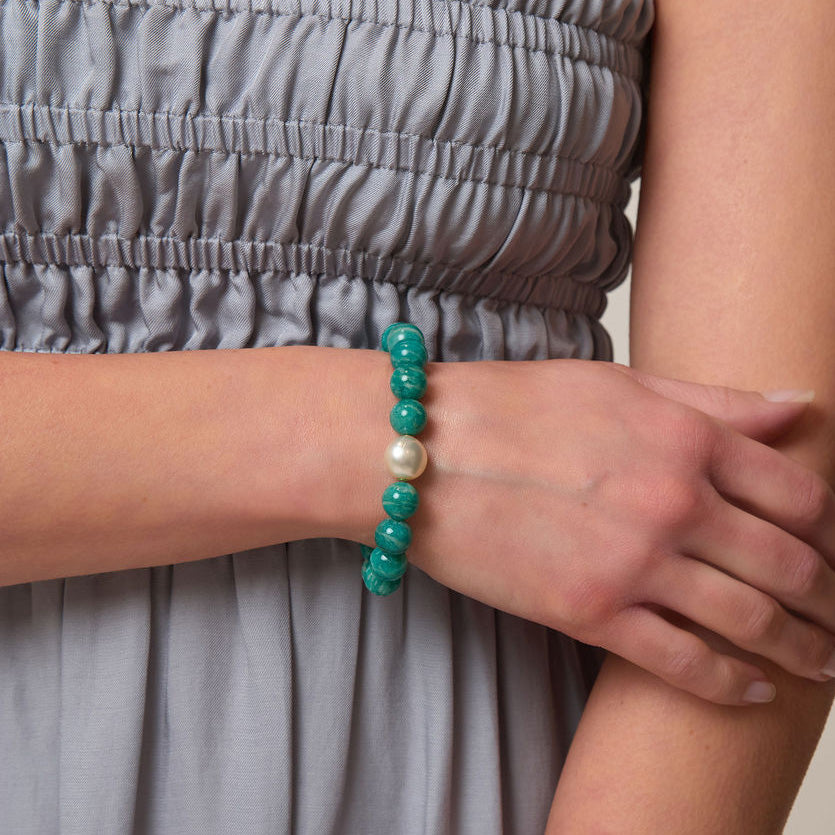 Person wearing a bracelet with green beads and a pearl on a neutral background