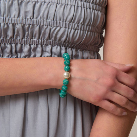 Person wearing a bracelet with green beads and a pearl on a neutral background