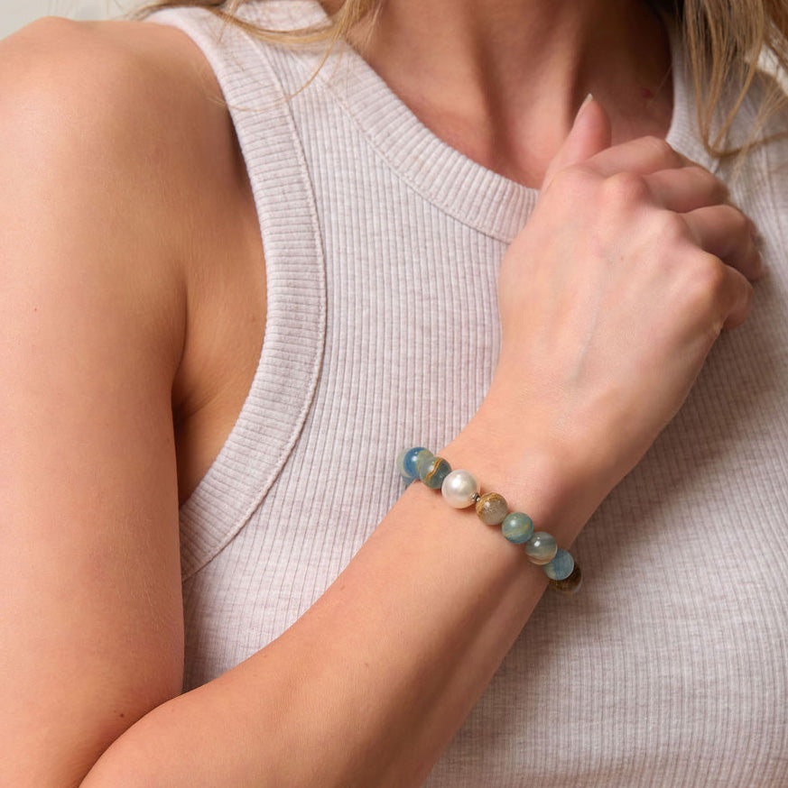 Close-up of a person wearing a blue beaded bracelet and a pearl on a neutral background