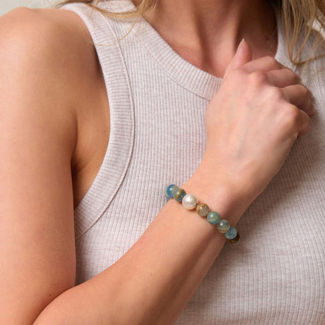 Close-up of a person wearing a blue beaded bracelet and a pearl on a neutral background