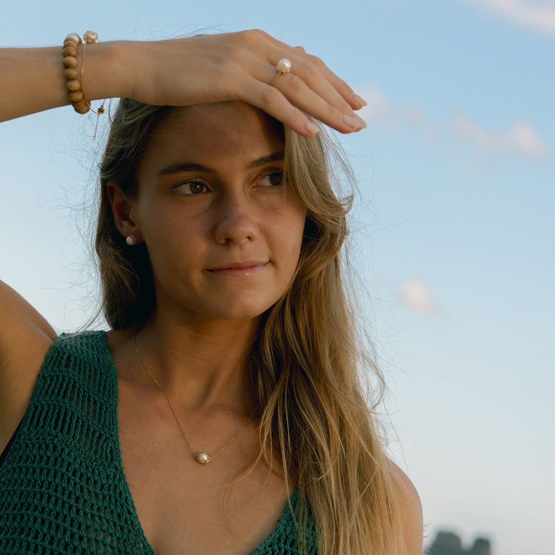 Woman with a green top and pearl jewelry against a blurred natural background