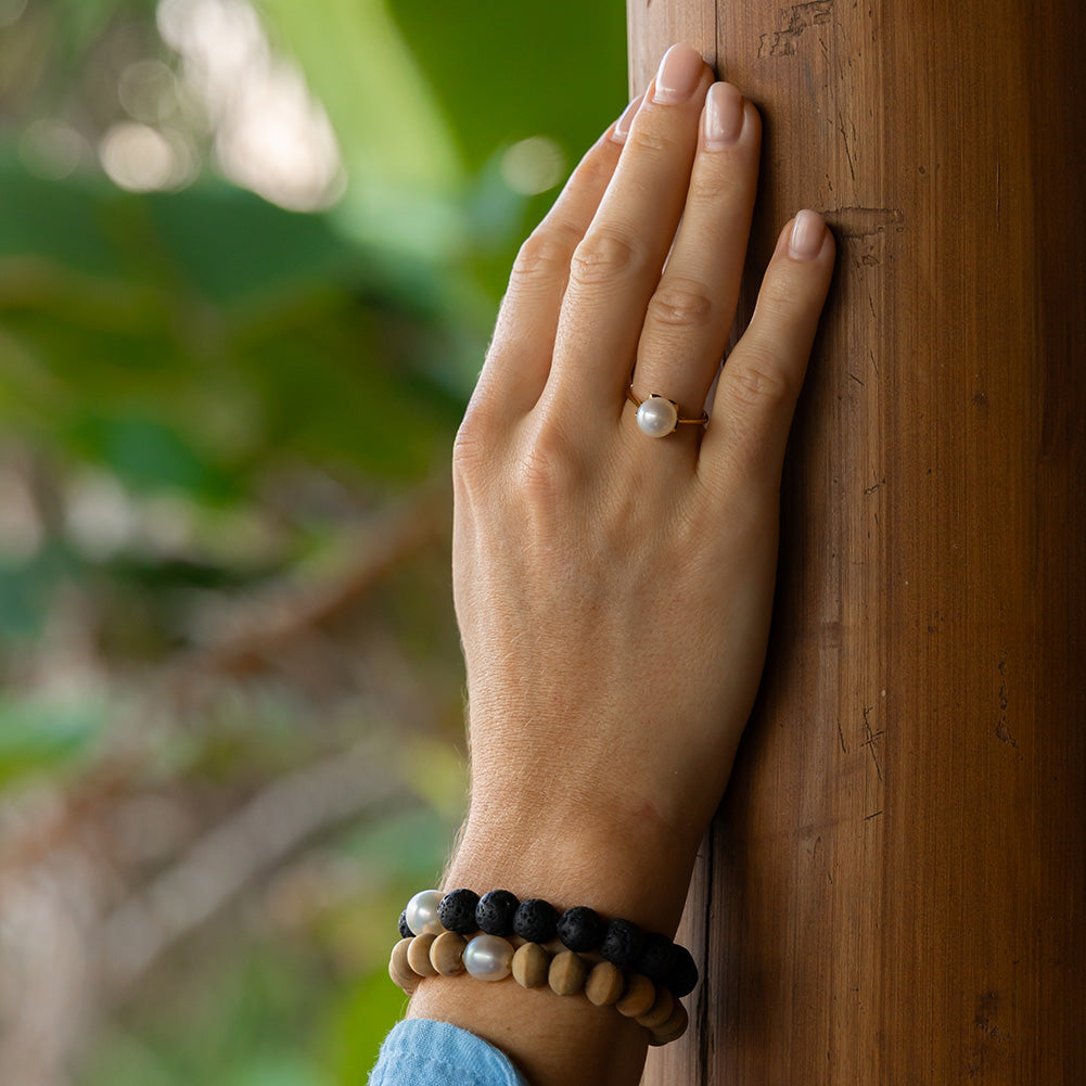 Hand with a pearl ring and beaded bracelets against a wooden background