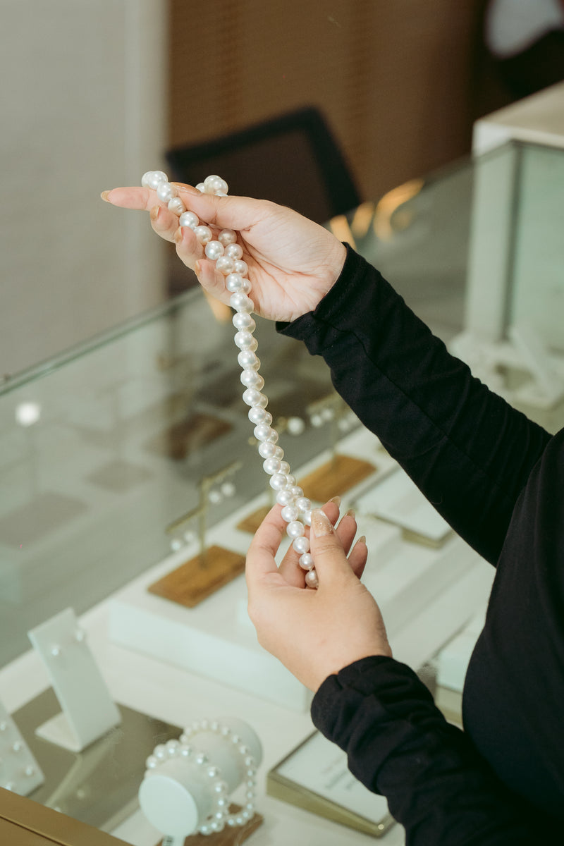 Person holding a pearl necklace in a jewelry store.