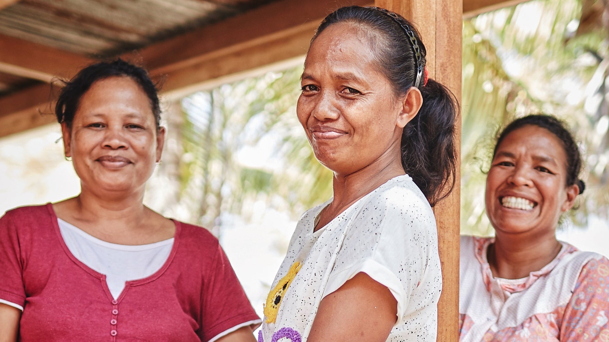 Three women sitting together under a wooden shelter with a natural background.