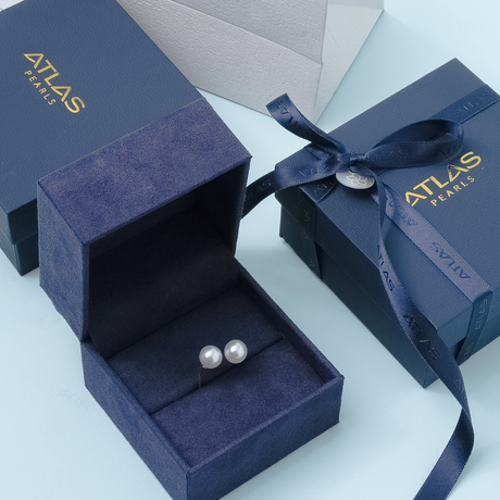 Pearl earrings in an Atlas Pearls box on a light blue background