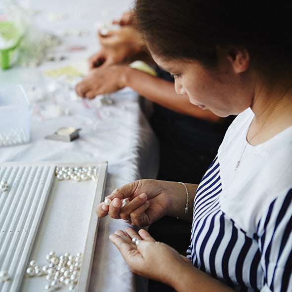 Two people working on pearl grading with tools on a table.