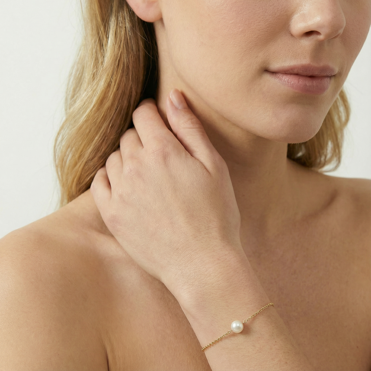 Woman wearing a delicate gold bracelet with a pearl on a plain background