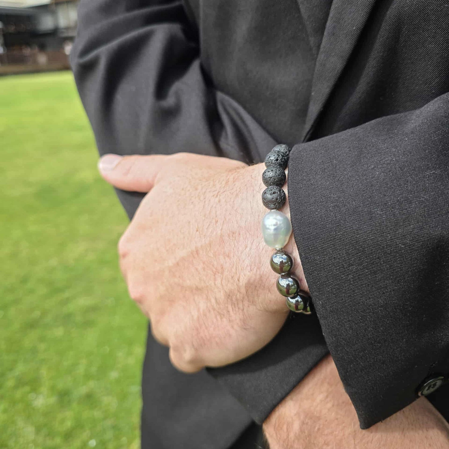 Person wearing a black beaded bracelet with a blurred grassy background