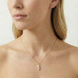 Close-up of a woman wearing a gold necklace with a pearl pendant on a neutral background