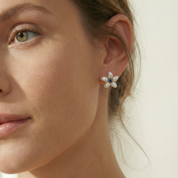 Close-up of a woman wearing a floral earring with pearls and a blue gemstone.