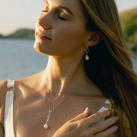 Woman wearing pearl earrings and necklace by a body of water