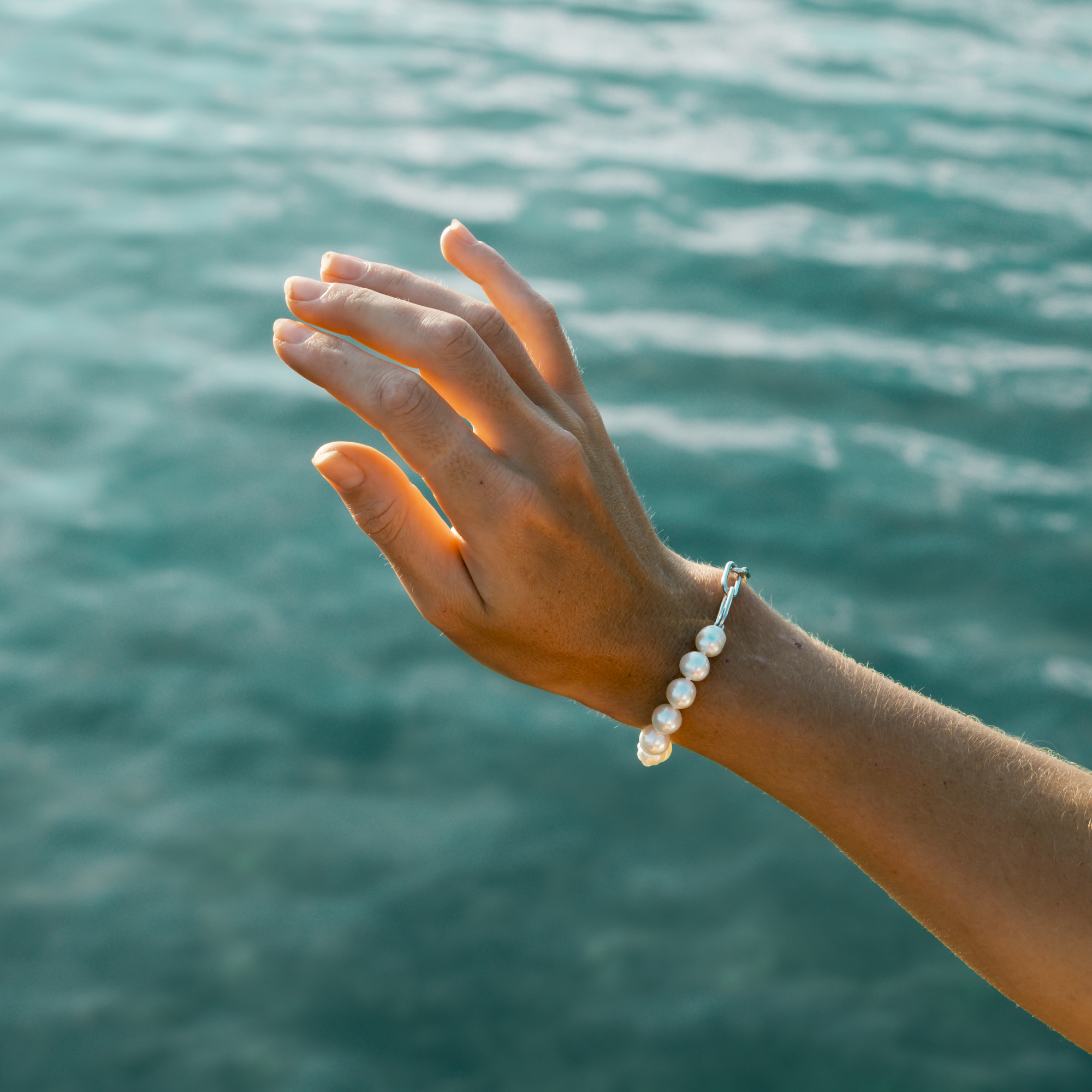 Hand wearing a pearl bracelet with water in the background