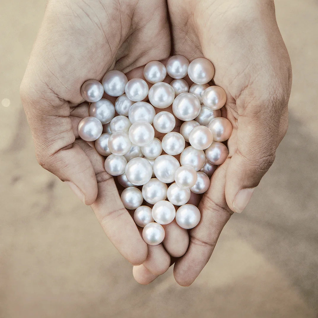 Hands holding numerous pearls on a blurred sandy background 