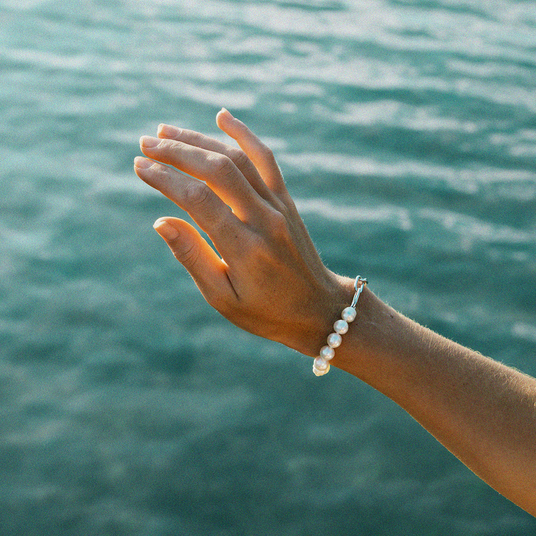 Hand wearing a pearl bracelet with a blurred water background