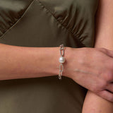 Person wearing a silver bracelet with a pearl on an olive green background