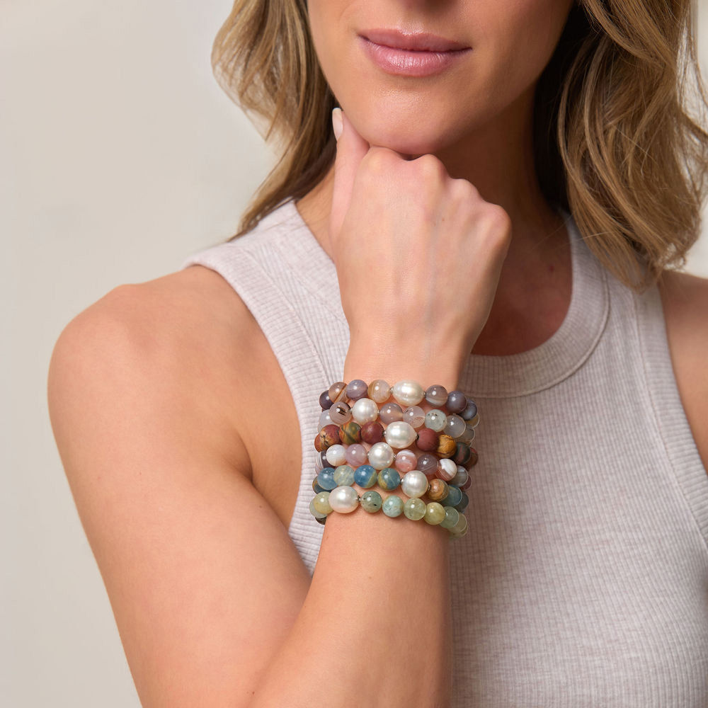 Woman wearing a stack of colorful beaded bracelets on a neutral background
