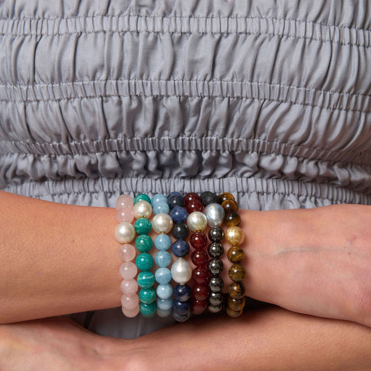 Stack of beaded bracelets on a wrist with a gray garment in the background