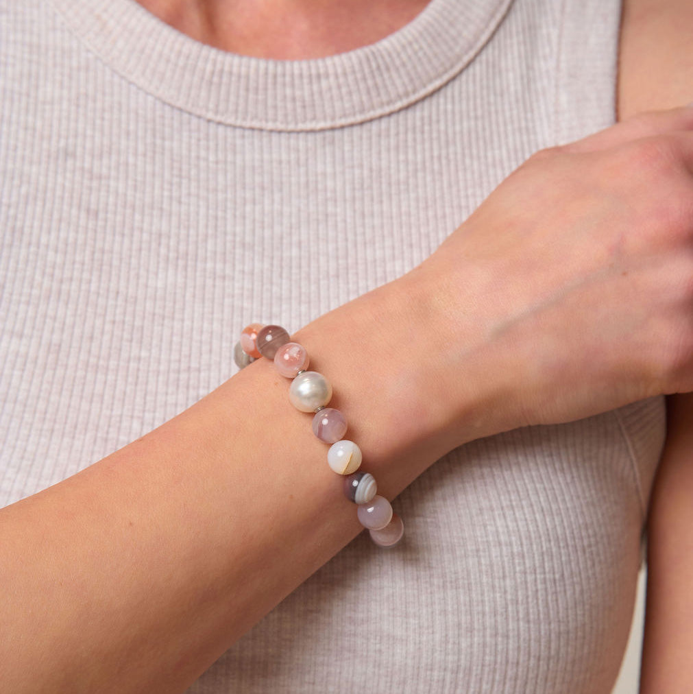 Person wearing a bracelet with multicolored pink beads on a plain background