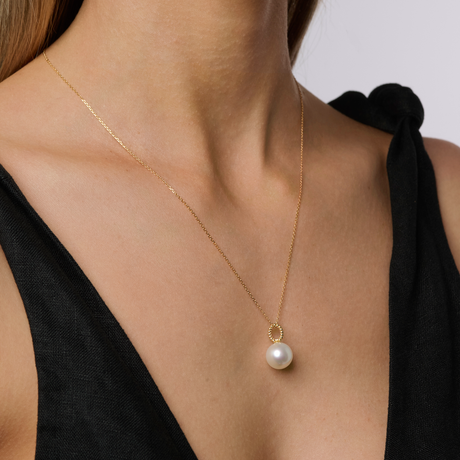 Gold necklace with a pearl pendant on a person wearing a black top.