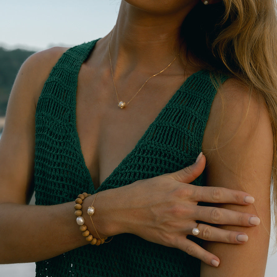 Woman wearing a green sleeveless top with a blurred background. Modelling a necklace, ring and stack of bracelets. 