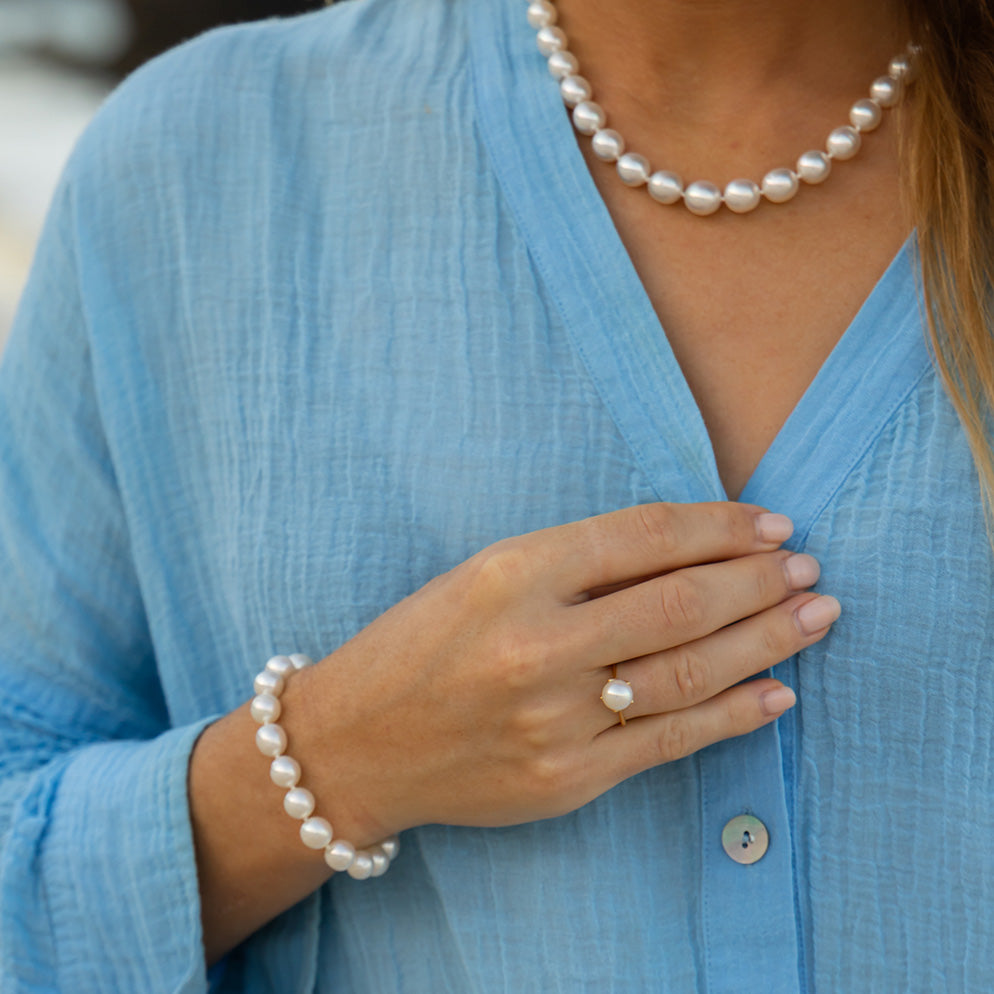 Person wearing a blue shirt with pearl jewelry including a necklace, bracelet, and ring.