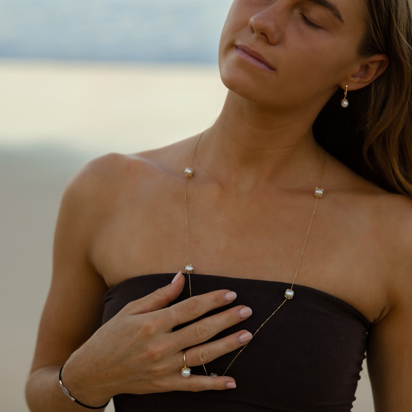 Woman wearing a delicate necklace with small pendants against a blurred natural background
