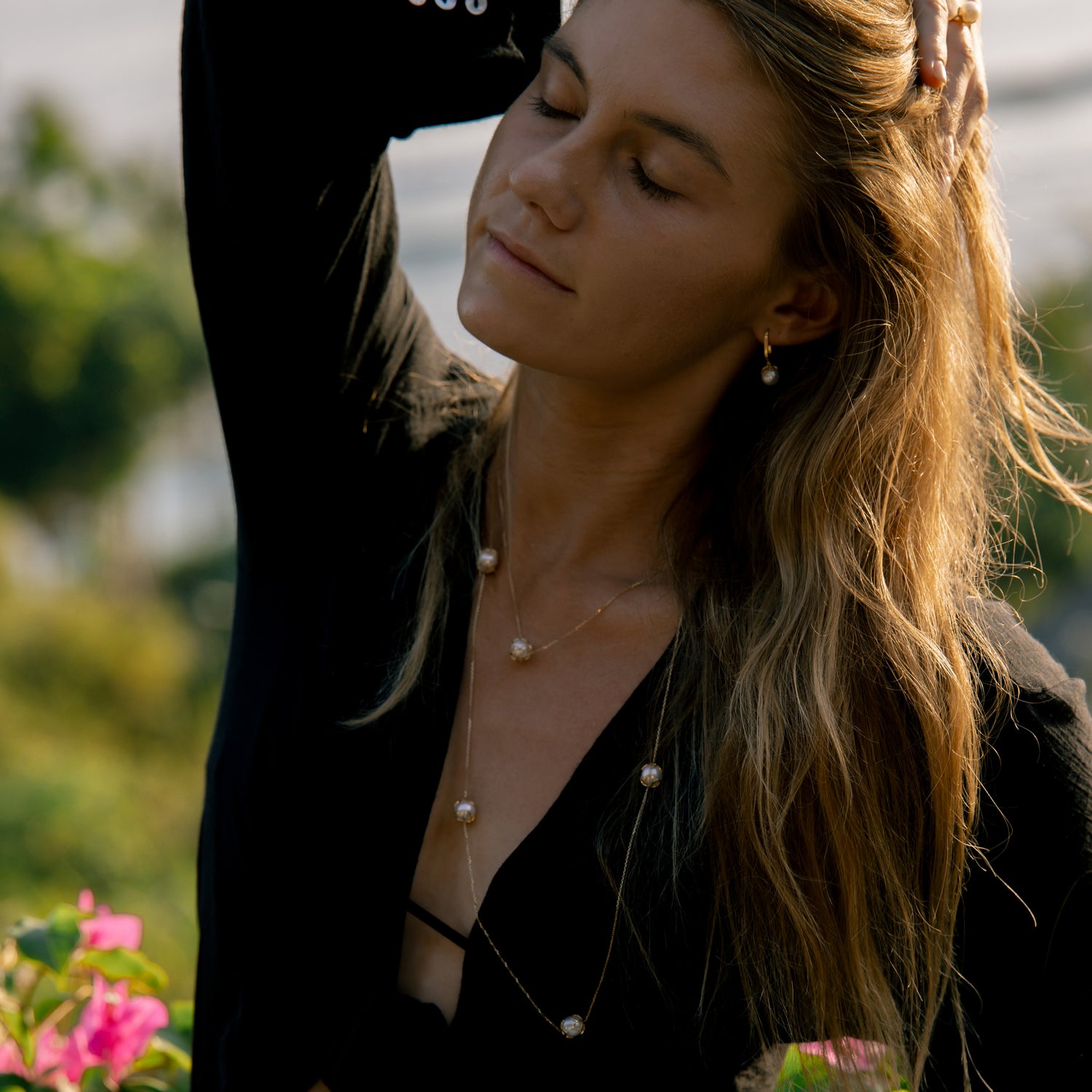 Woman with long hair and pearl necklace standing outdoors with blurred background