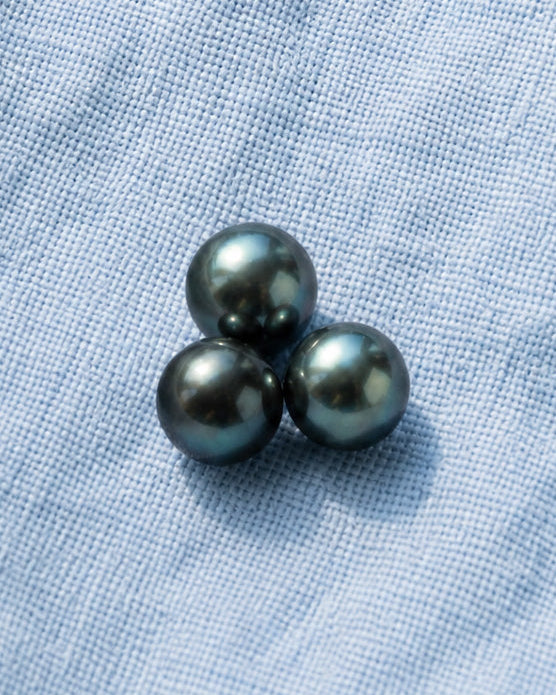 Three black pearls on a textured blue fabric background